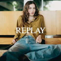 Mladá žena v olivově zelené košili a modrých džínách, sedící na podlaze a opírající se o dřevěnou skříň uvnitř.