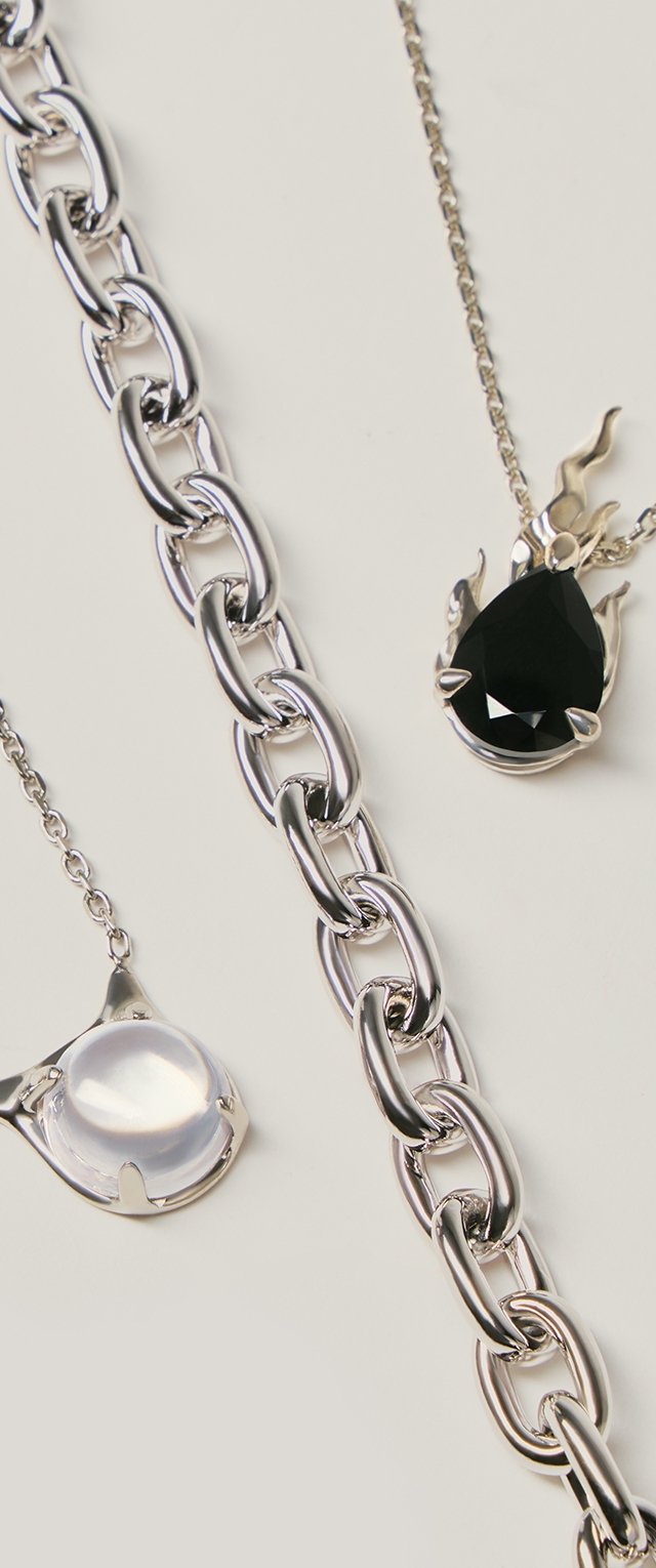 Sidabrinė grandinėlės apyrankė ir du sidabriniai kaklo papuošalai su pakabukais – vienas juodas lašo formos su liepsnos motyvu, kitas permatomas apvalus akmuo su katės ausų formos apvadais.