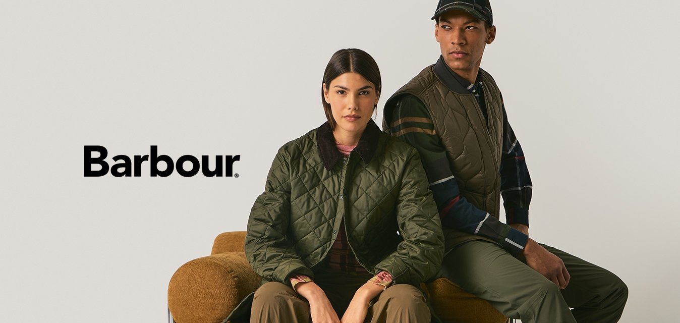 Dvě osoby v olivově zelených prošívaných svrchních oděvech sedící na hnědém texturovaném křesle před jednobarevným béžovým pozadím.