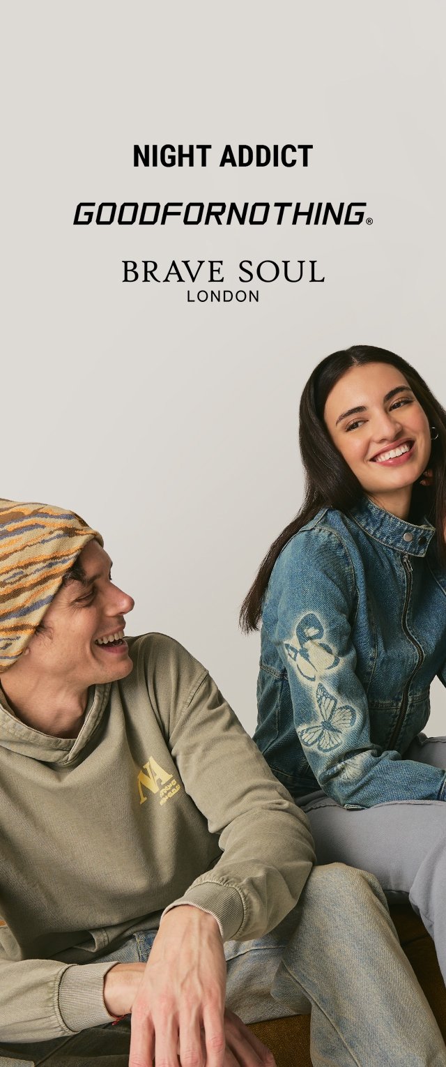 Dos personas están sentadas. Una lleva una sudadera con capucha verde oliva claro con un logo; la otra lleva una chaqueta vaquera con bordados florales y pantalones grises.