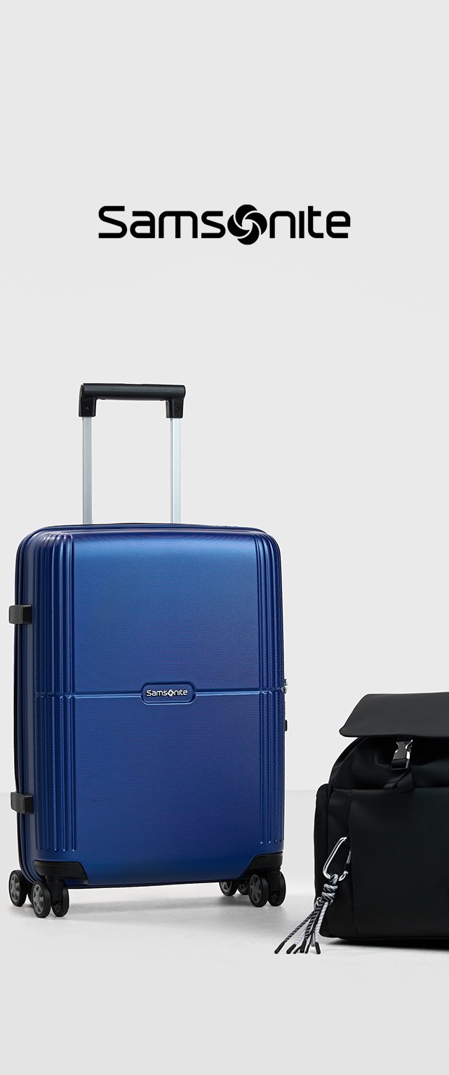 Maleta rígida azul con textura estriada, mango retráctil y cuatro ruedas. Junto a ella hay una bolsa de deporte negra de tela suave con una solapa superior.