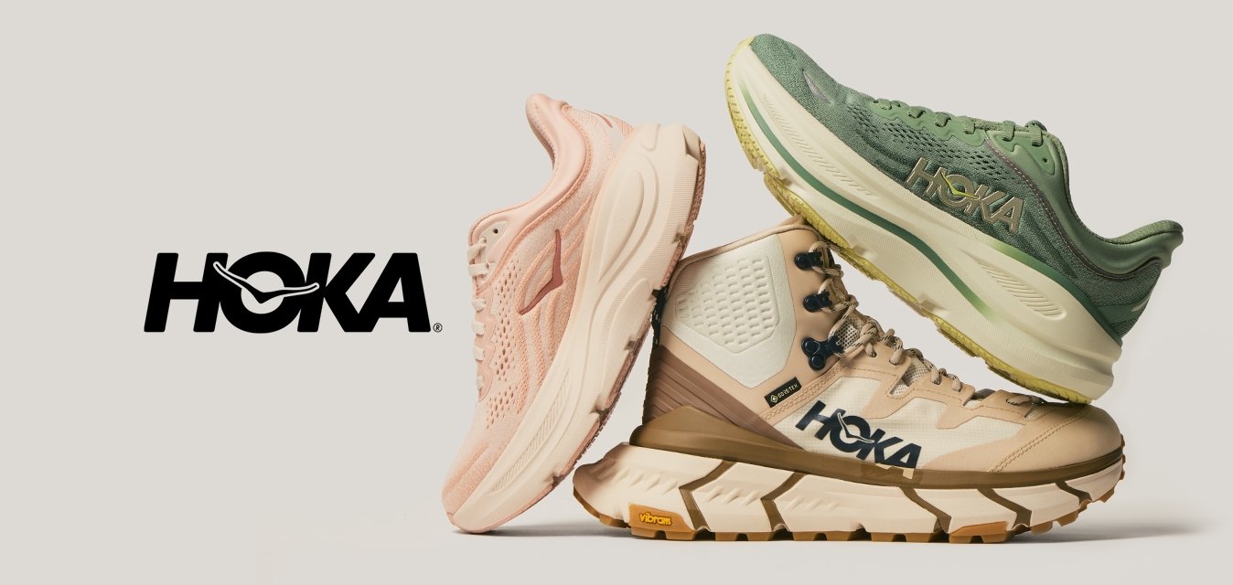 Tři poskládané běžecké boty HOKA v růžové, béžové turistické boty a zelené v bočním pohledu na světle neutrálním pozadí.