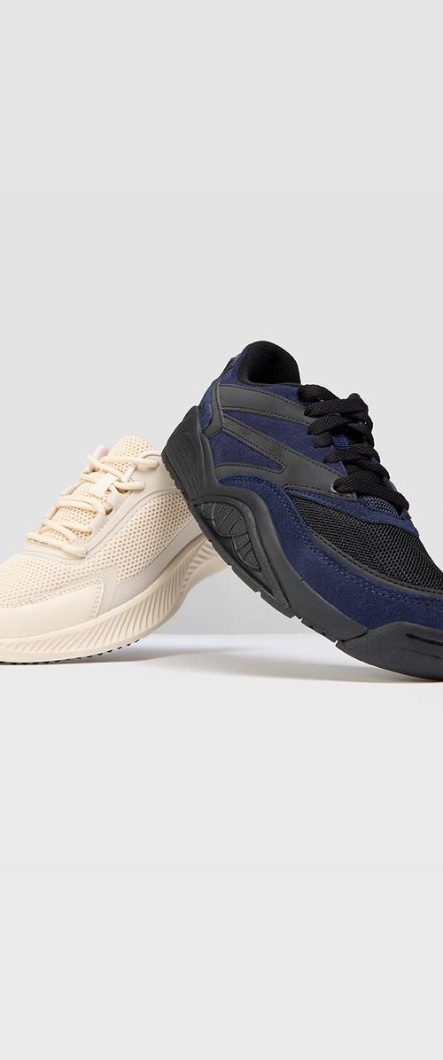 Zapatillas deportivas que presentan una parte superior de malla beige con acentos texturizados y una parte superior azul marino con paneles lisos y de malla. Suelas de goma con dibujo.