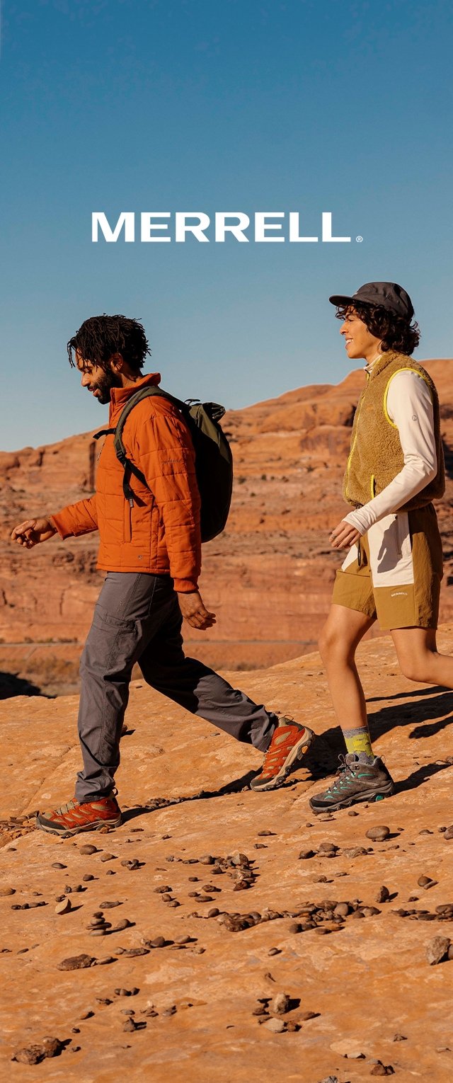 Due escursionisti su un terreno roccioso. Uno indossa una giacca isolante arancione e pantaloni grigi, l'altro un gilet giallo e pantaloni corti beige. Entrambi hanno zaini.