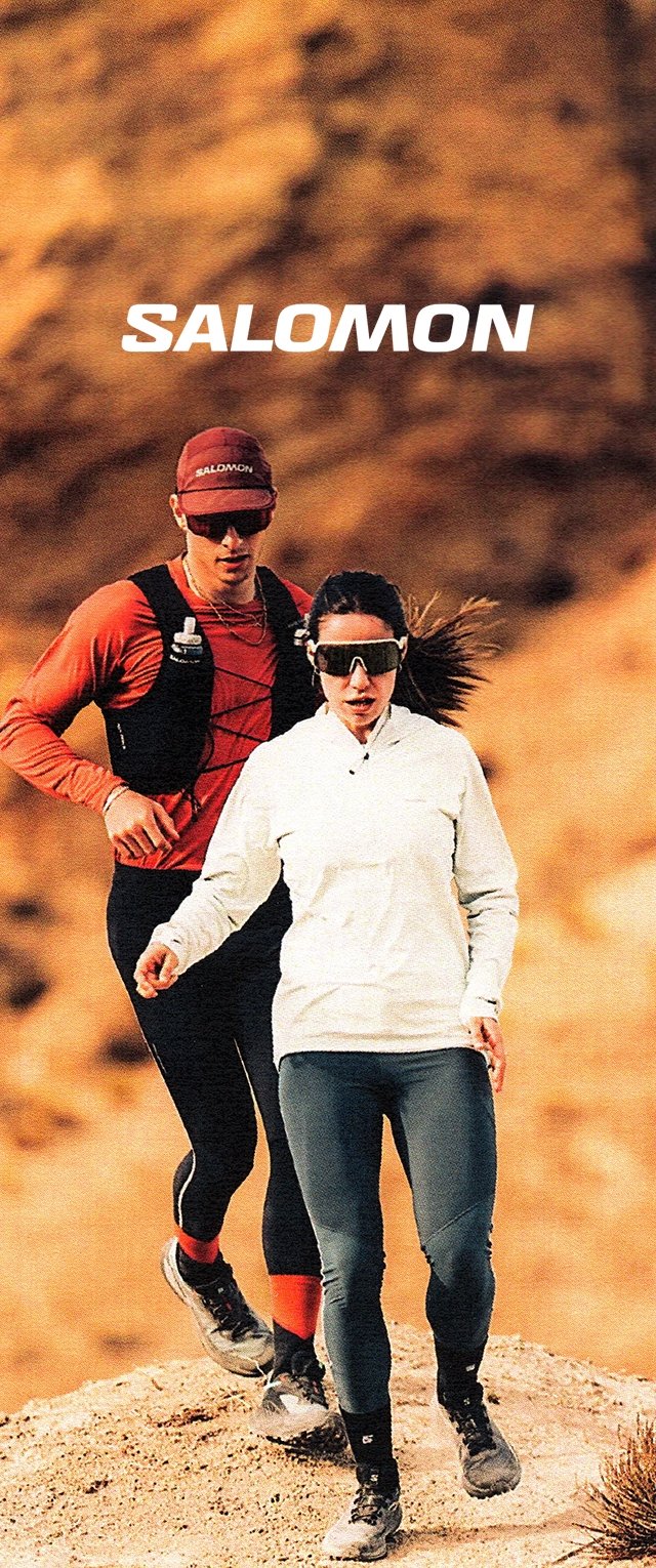 Due corridori su un terreno roccioso. Uno indossa un top rosso, un gilet nero e un cappellino. L'altro indossa una giacca bianca e leggings neri aderenti.