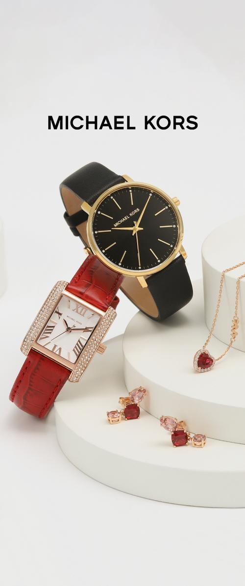 Zwei Michael Kors Uhren: eine runde in Schwarz und Gold, die andere rechteckig mit einem roten Krokodilarmband und Kristallakzenten. Außerdem pinke und rote Ohrringe.