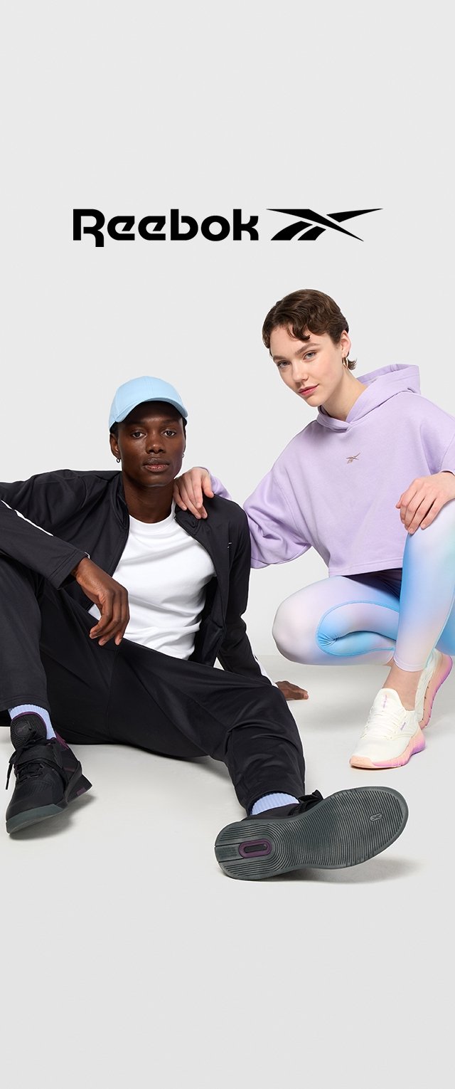 La ropa de Reebok incluye un chándal negro, una gorra azul clara, un hoodie corto lavanda y leggings en degradado pastel, acentuados por unas zapatillas blancas y rosas.