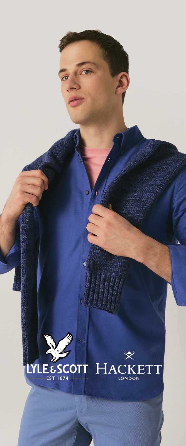 Blå skjorte i bomull med knapper, lagdelt med en mørkeblå strikket genser drapert over skuldrene. Lys rosa undertrøye er synlig.