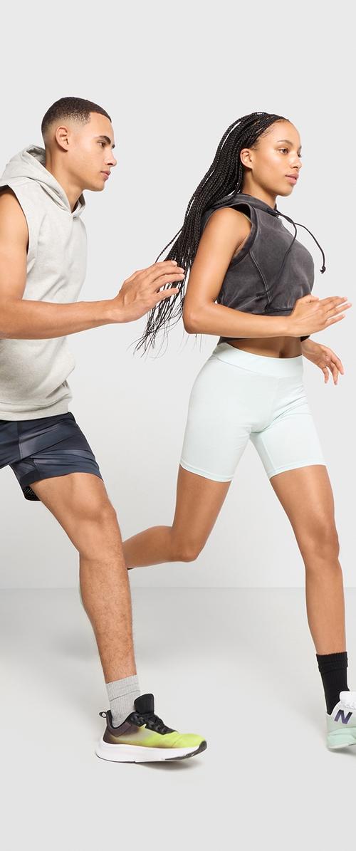 Due persone stanno correndo. Una indossa un hoodie grigio senza maniche e pantaloni corti scuri, mentre l'altra indossa un crop top nero e pantaloni corti azzurri.