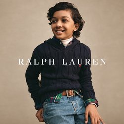 Chlapec s tmavými kudrnatými vlasy, oblečený v tmavě modrém svetru přes kostkovanou košili a džíny, usmívající se a dívající se stranou na jednobarevném pozadí.