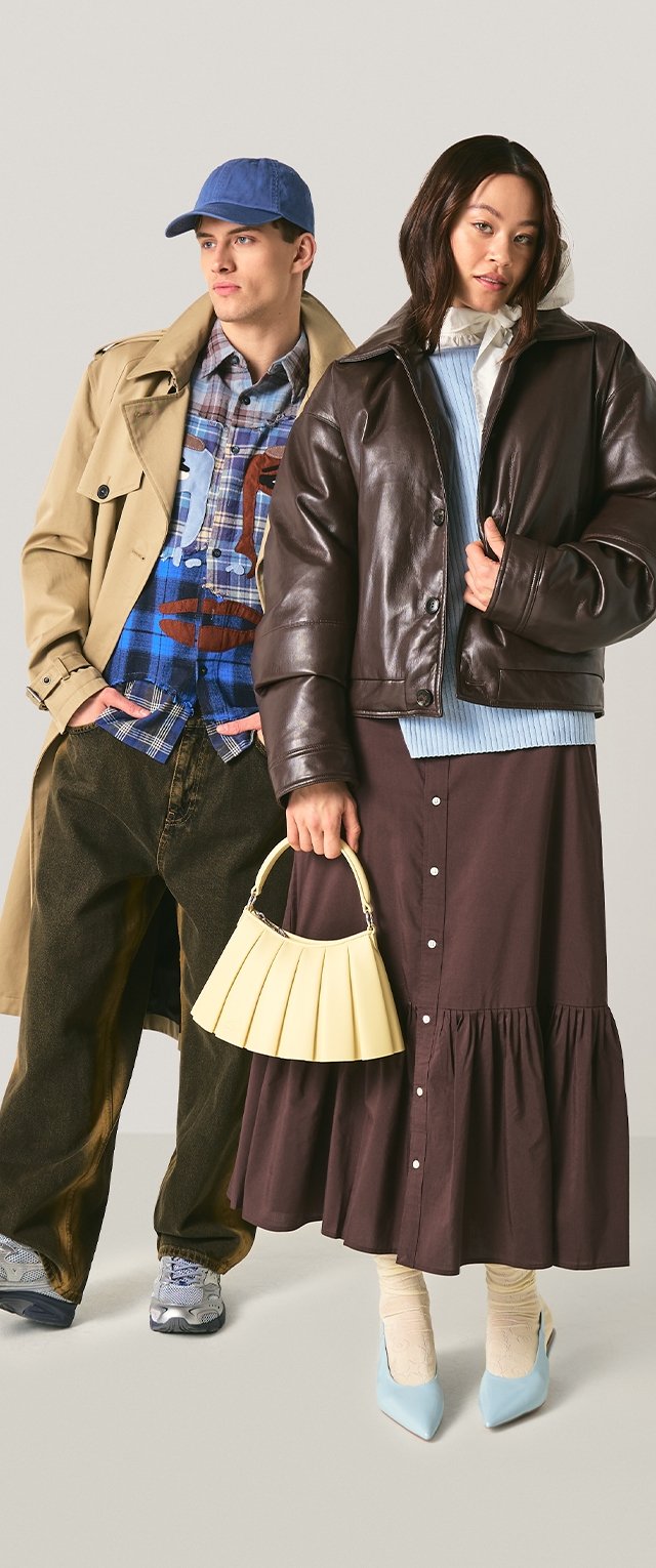 Joven con abrigo beige, gorra azul, camiseta gráfica y pantalones oscuros; joven con chaqueta de cuero marrón, suéter azul, falda larga y bolso crema.