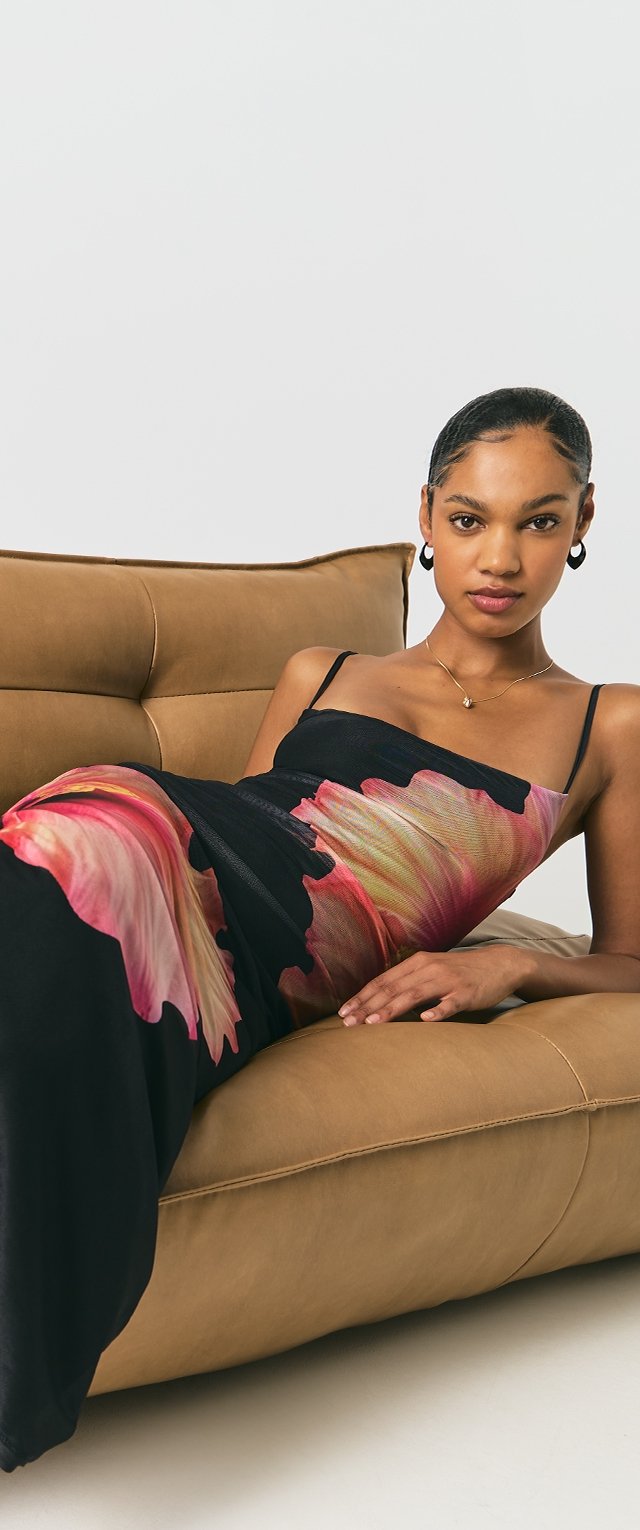 Vestido negro con estampado floral vibrante en rosa, tirantes finos, tejido suave y corte relajado, combinado con un sofá de cuero marrón.