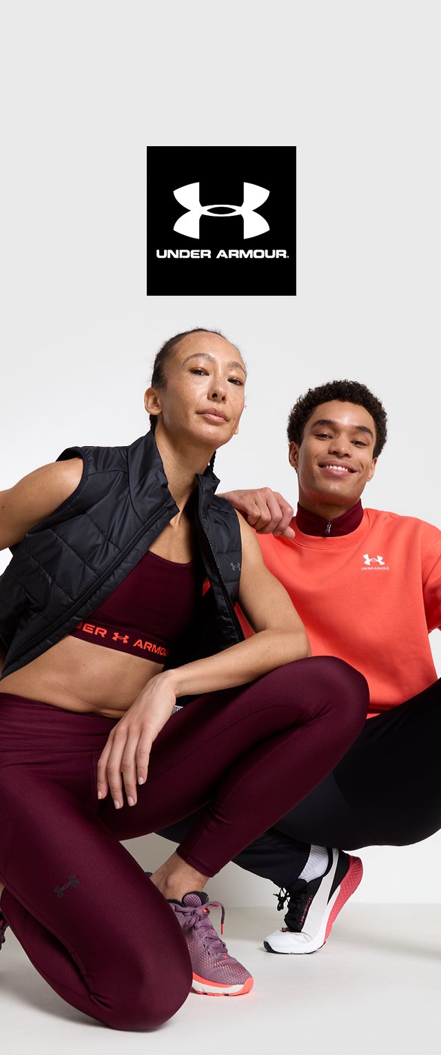 Czarna kamizelka puchowa, bordowy stanik sportowy i legginsy. Pomarańczowy sweter. Czarno-białe sneakersy. Logo Under Armour wyświetlone na górze.
