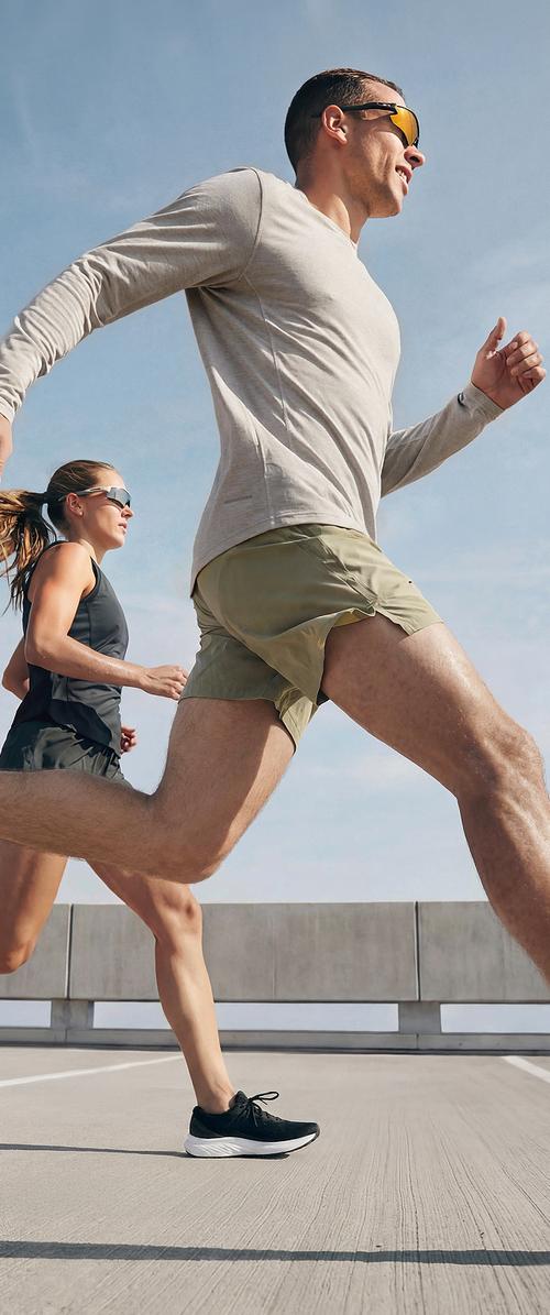 Un homme et une femme portant des lunettes de soleil courent à l'extérieur sur une surface en béton sous un ciel dégagé.