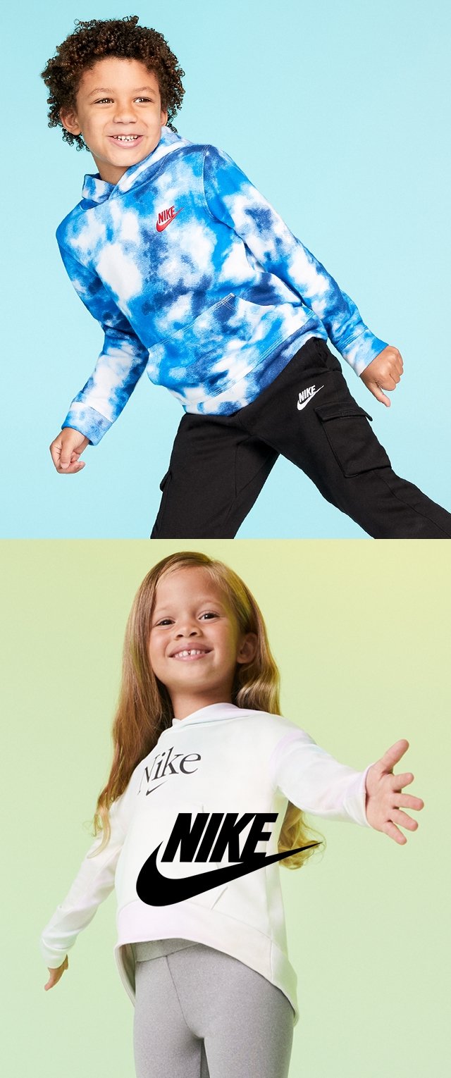 Dos niños llevan ropa de Nike. El niño tiene una sudadera azul con patrón de tie-dye y un logo rojo, mientras que la niña viste una camiseta blanca con un logo negro. Ambos llevan pantalones en negro y gris.