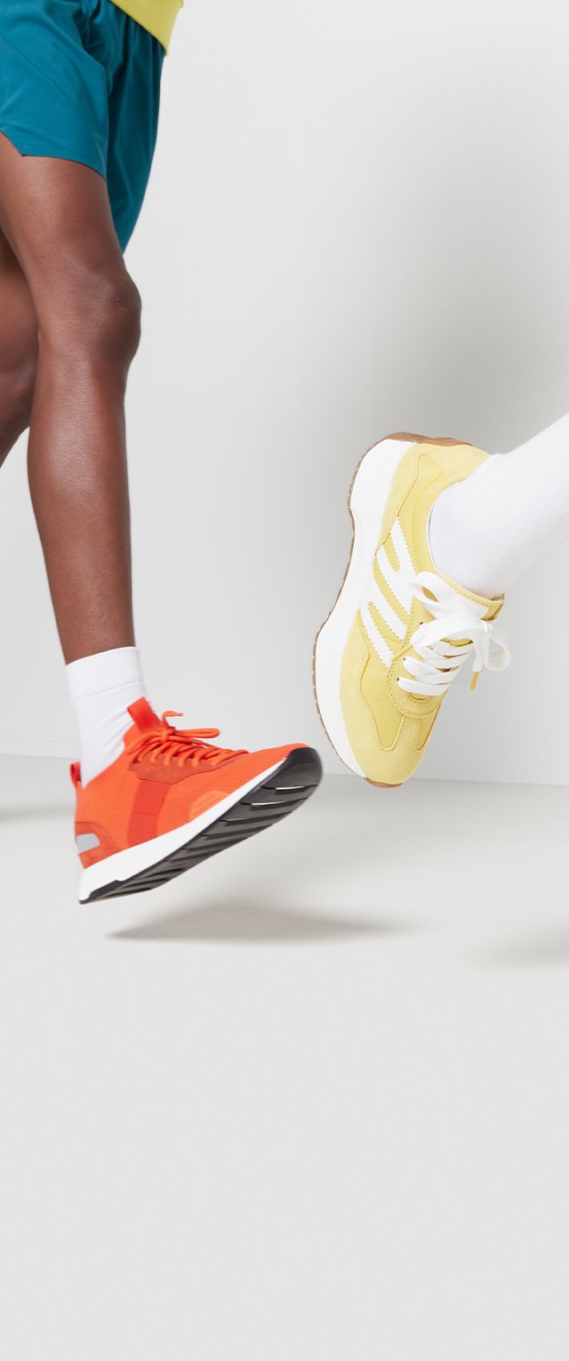 Oranje sportieve sneaker met mesh-panelen, zwarte zool en reflecterende accenten, naast een gele vetersneaker met witte strepen.