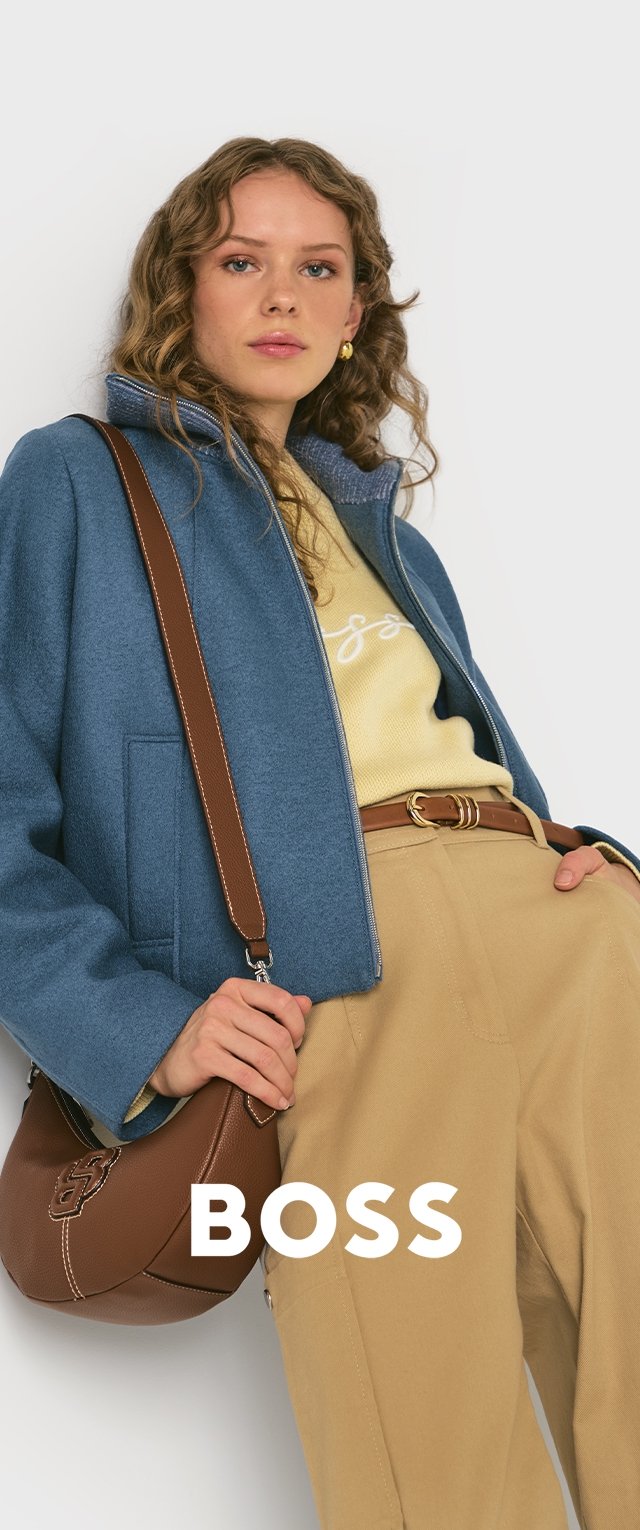 Veste zippée bleue sur un pull jaune, associée à un pantalon beige. Sac bandoulière marron avec détails de logo et bandoulière en cuir.