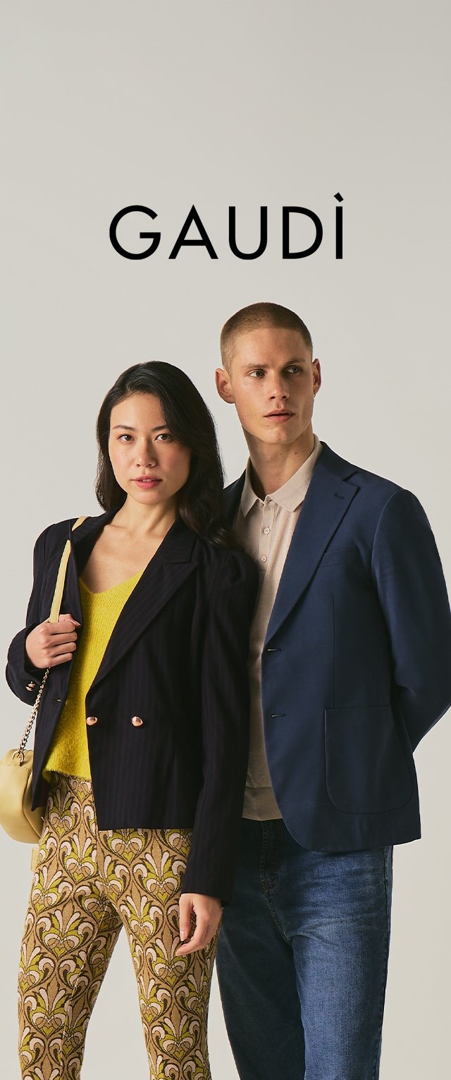 Mujer con pantalones estampados, blusa amarilla, blazer negra y bolso; hombre con blazer azul, camisa beige, vaqueros, de pie frente a un fondo liso con el texto "GAUDÌ" arriba.