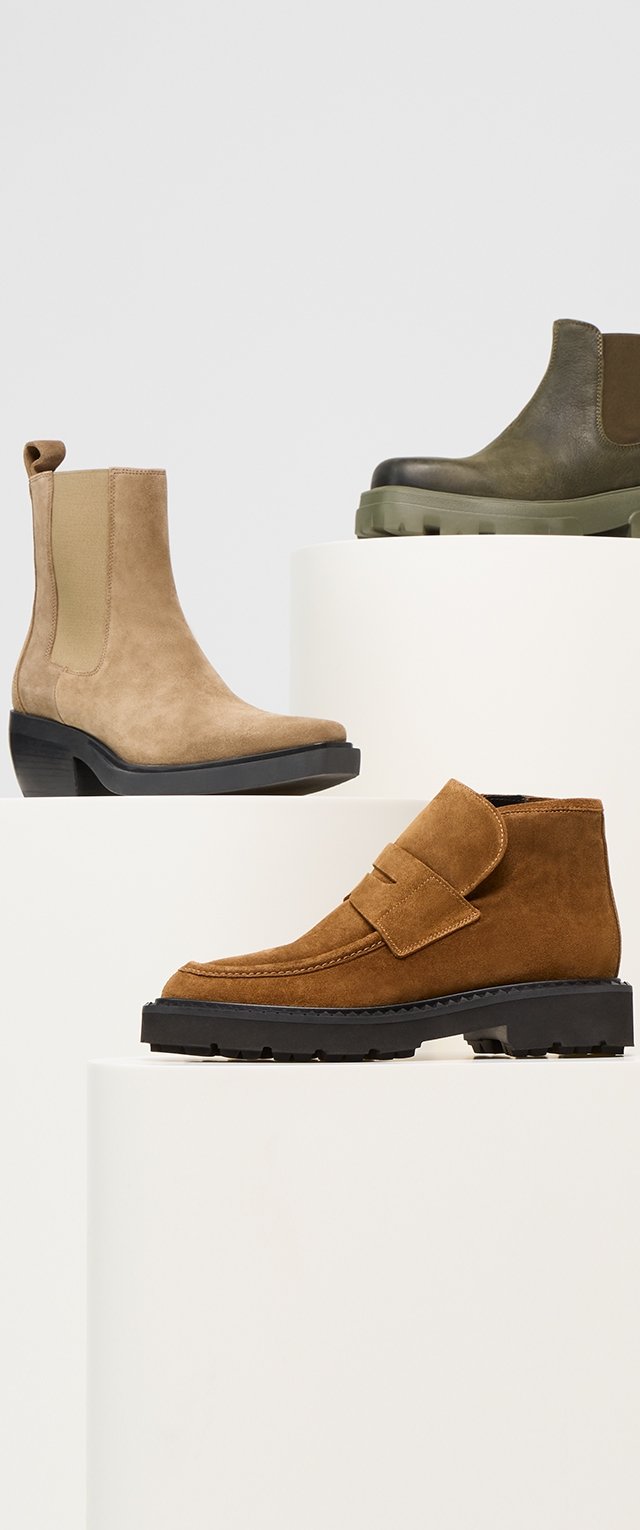 Tres pares de botas exhibidos en pedestales blancos: una bota de tobillo de ante color marrón, una bota de cuero verde con una suela gruesa, y un zapato de ante marrón con una correa.