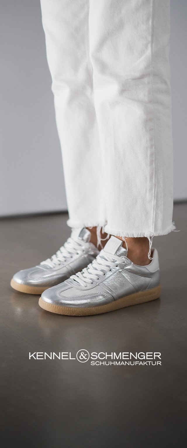 Zapatillas de cuero plateadas con una textura suave, cordones blancos y una suela de goma marrón clara, combinadas con jeans blancos deshilachados.