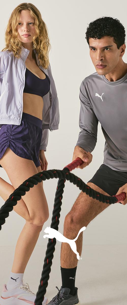 Mujer y hombre con ropa deportiva usando cuerdas de batalla para hacer ejercicio sobre un fondo liso.