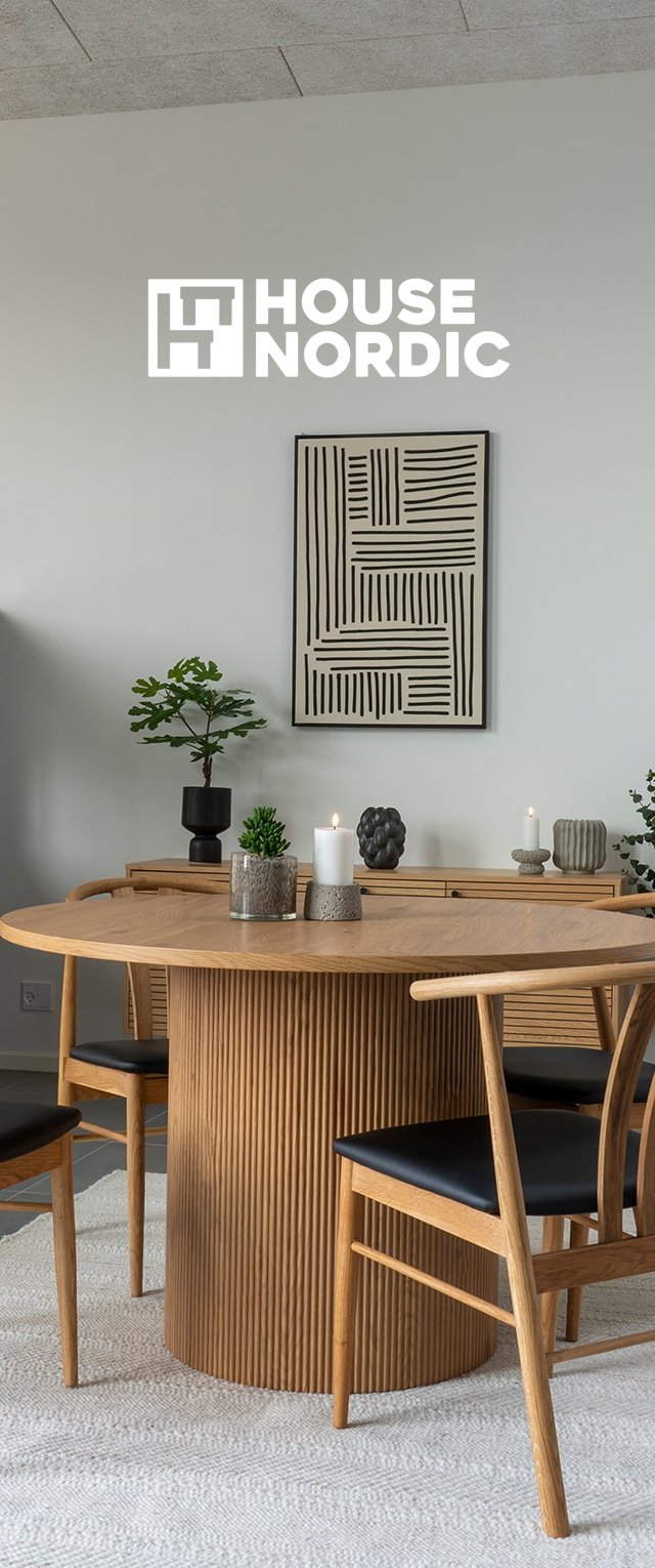 Mesa de comedor redonda de madera con cuatro sillas de madera con cojines negros, velas, plantas verdes y arte mural abstracto en blanco y negro en una habitación minimalista.