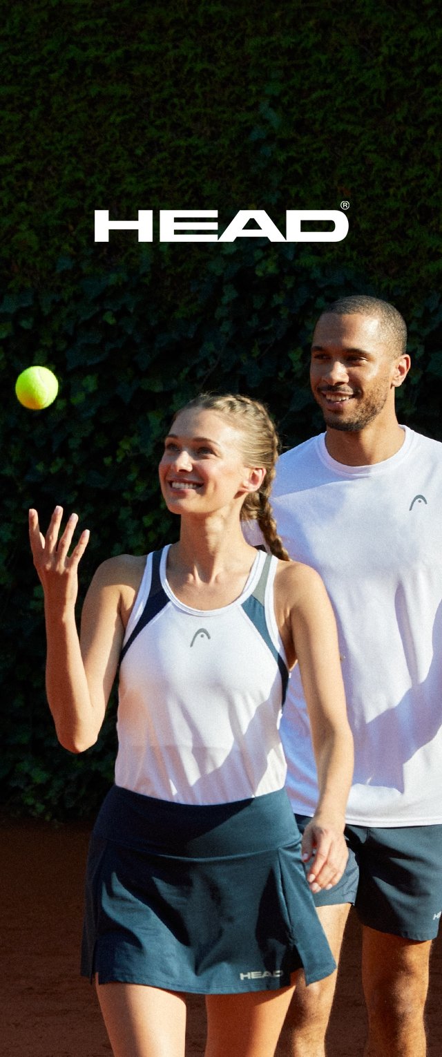 Dos personas en una cancha de tenis, vestidas con ropa deportiva blanca y azul marino. La mujer sostiene una pelota de tenis, sonriendo, mientras el hombre camina a su lado.