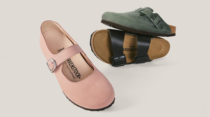 Pinkfarbener Mary-Jane-Schuh mit Schnalle vorne und zwei Slip-On-Sandalen, eine schwarze mit doppelten Riemen, eine grüne mit einem einzelnen Riemen, alle auf hellem Hintergrund.
