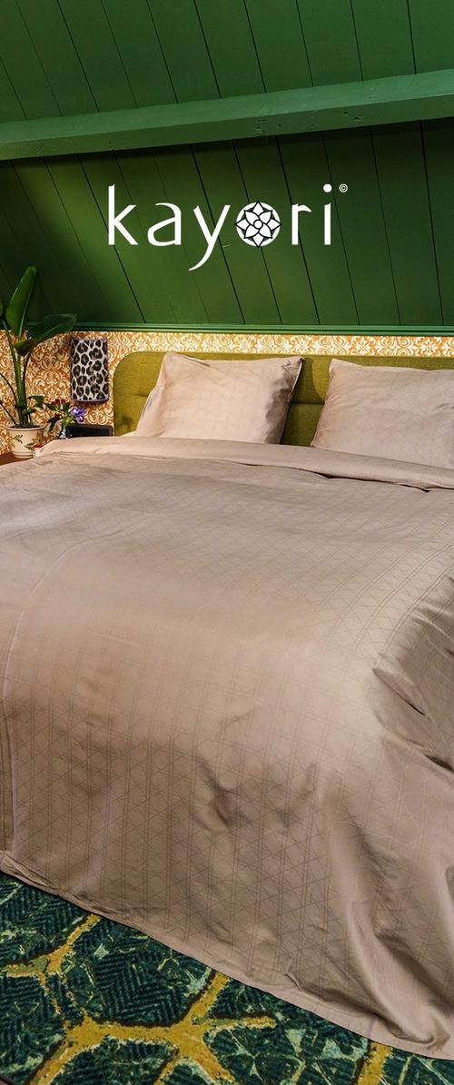 Bettwäsche-Set in hellem Taupe mit einem geometrischen Muster auf der Bettdecke. Weicher Stoff über dem grünen gepolsterten Kopfteil und einem strukturierten Teppich.