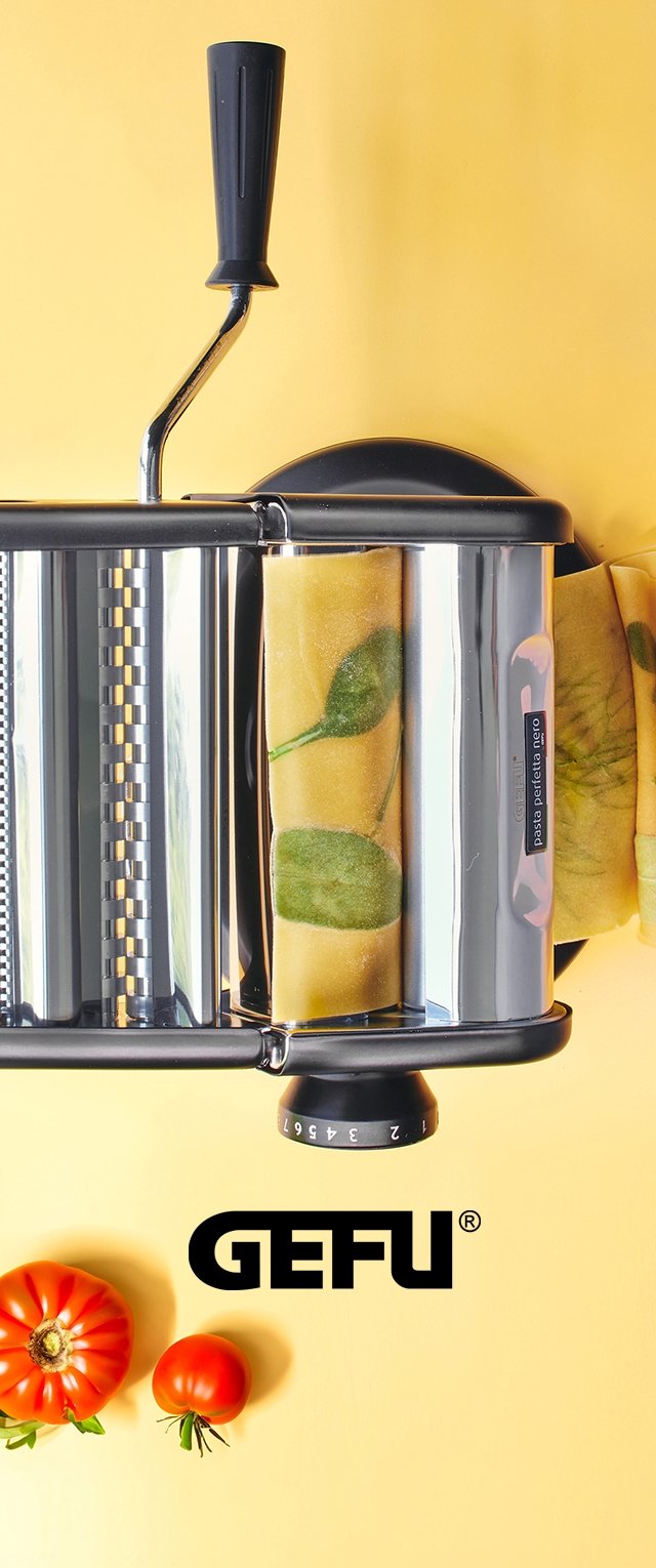 Macchina per pasta in metallo con manico nero, corpo argentato e impostazioni di spessore regolabili. Include sfoglie di pasta gialle con motivi a foglia verde.