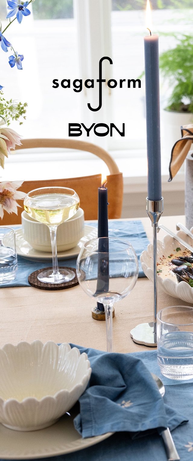 Borddekking med blå taperlys, en kremfarget skål med bølget kant, glassware, et lyseblått duk, og blomsterdekorasjoner.