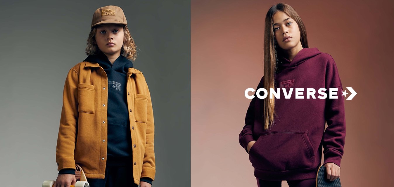 Dvě děti pózují se skateboardy. Chlapec má na sobě hořčičnou bundu přes námořnickou mikinu; dívka má na sobě burgundskou mikinu se sladěnými legínami.