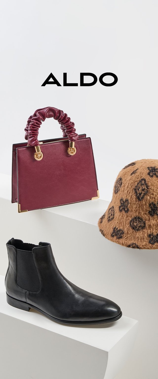 Zwarte leren enkelboot met elastische zijkanten, bordeaux handtas met geplooide handgreep, en tan emmerhoed met donker bloemenpatroon.