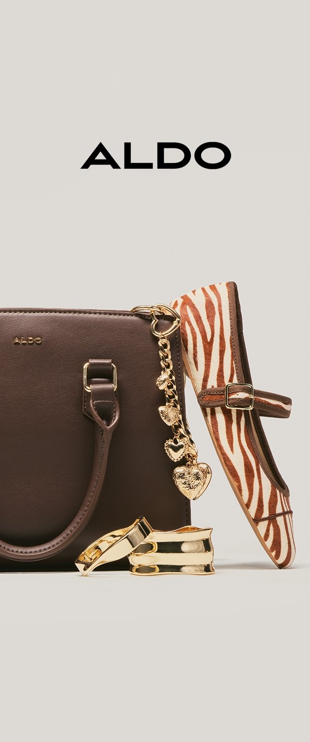 Tummanruskea käsilaukku, jossa on kulta sydänriipusketju, seepraraidallinen tasainen kenkä soljella ja kaksi kultasormusta beigen taustan päällä.