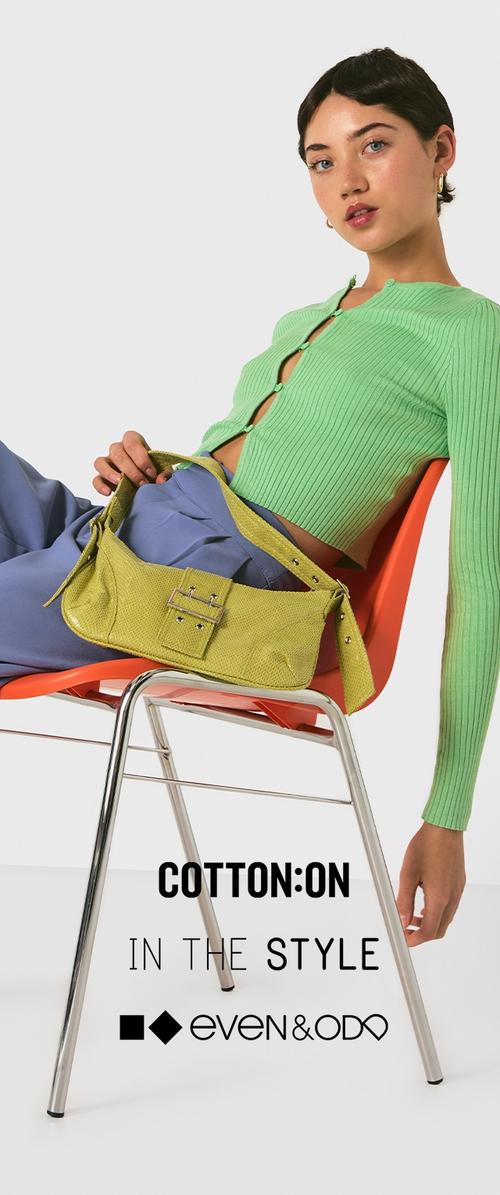 Cardigan verde acanalado, pantalones azul claro y un bolso texturizado verde lima con detalle de hebilla, colocados sobre una silla plateada frente a un fondo blanco.