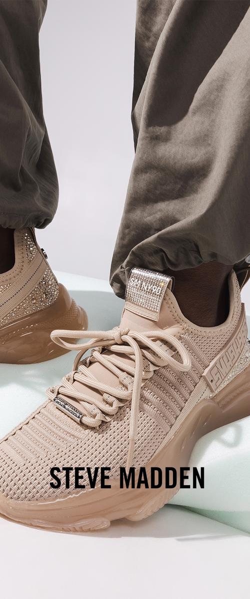 Beige stickade sneakers med tjocka sulor, dekorativa strassstenar och märkesspecifika detaljer, båda med vida byxor.