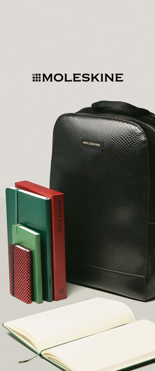Zaino in pelle nera testurizzata con logo dorato. Accanto ci sono un quaderno verde, un diario rosso, piccoli quaderni verdi e rossi e un planner bianco.