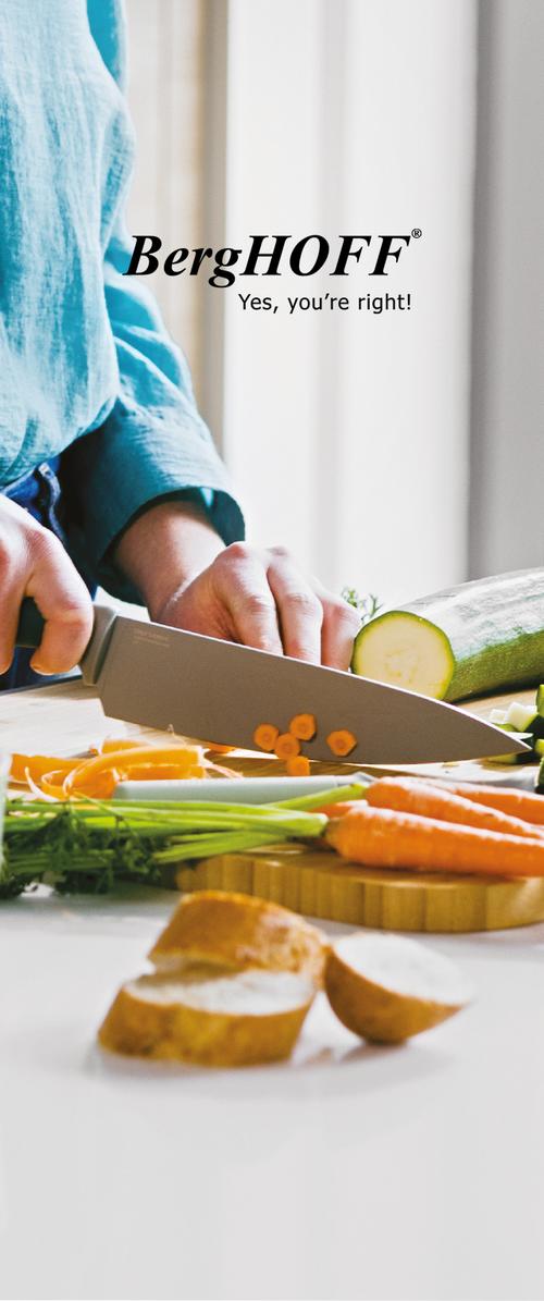 Personne en chemise bleue coupant des carottes et des courgettes sur une planche à découper en bois, avec du pain et des carottes tranchés visibles sur un comptoir blanc.