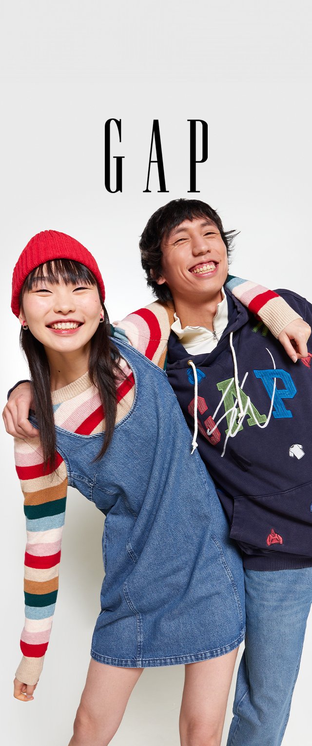 Twee personen poseren samen, de ene draagt een rode beanie en een denim jurk, de ander een marineblauwe hoodie met kleurrijke letters en een sweater.