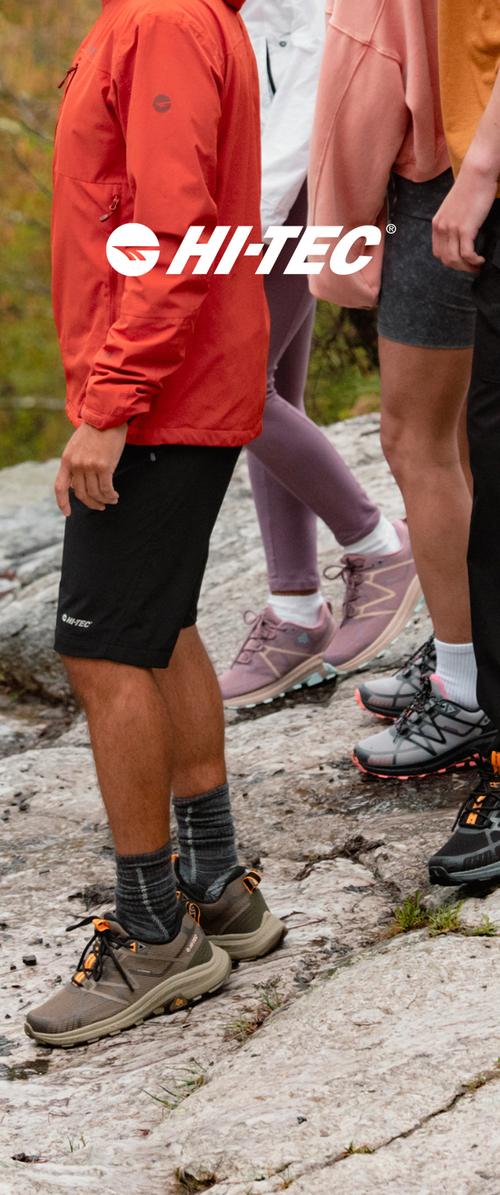 Vier Personen mit Outdoor-Ausrüstung und Hi-Tec-Schuhen stehen auf felsigem Gelände in einer natürlichen Umgebung.