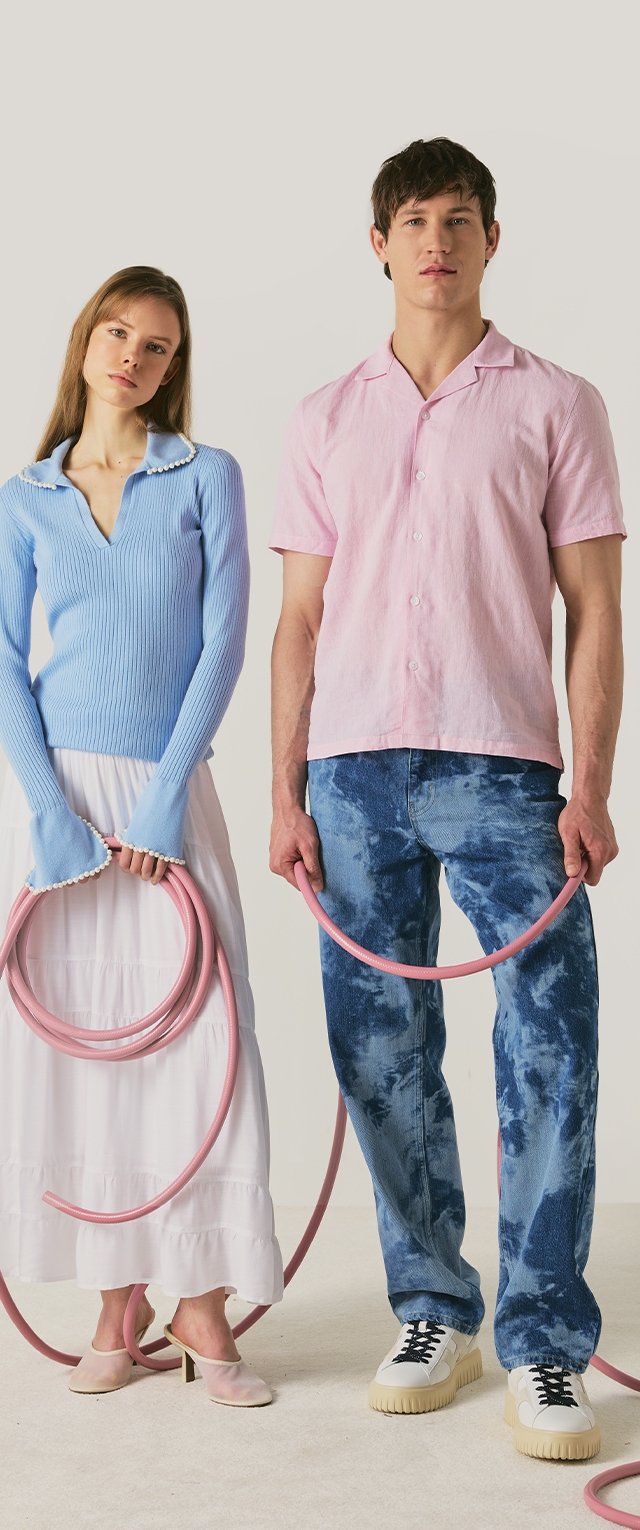 Een vrouw in een blauwe trui en witte rok en een man in een roze overhemd en blauwe spijkerbroek houden elk een roze tuinslang die voor hen is opgerold.