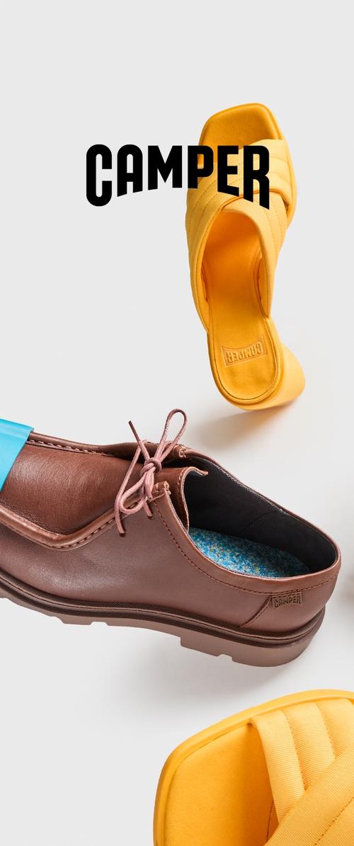 Scarpa in pelle marrone con accenti blu, dotata di lacci e suola testurizzata. Sandalo scivoloso giallo con cinturini larghi e soletta imbottita, entrambi marchiati "Camper."