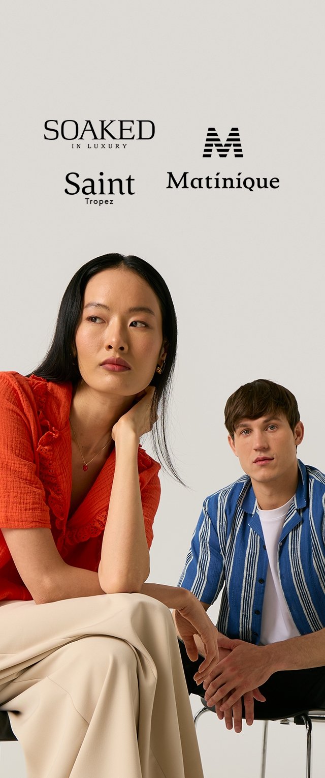 Dos modelos sentados, mujer con blusa roja y falda beige mira de lado, hombre con camisa azul de rayas y camiseta blanca se sienta detrás de ella, logos de marcas arriba.