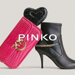 Černá kožená kotníková bota na vysokém podpatku se zlatým řetízkem vedle růžové texturované kabelky se zlatým logem a černého malého pouzdra ve tvaru srdce uvnitř.