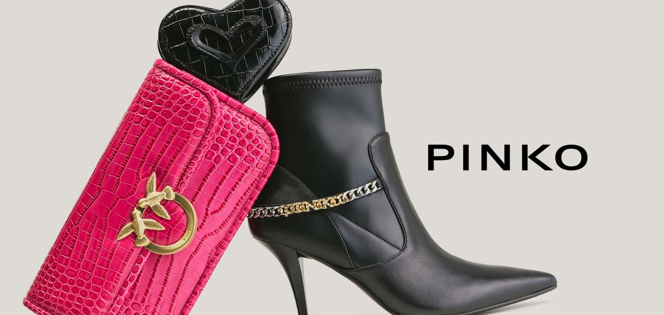 Černá kožená kotníková bota na vysokém podpatku se zlatým řetízkem vedle růžové texturované kabelky se zlatým logem a černého malého pouzdra ve tvaru srdce uvnitř.