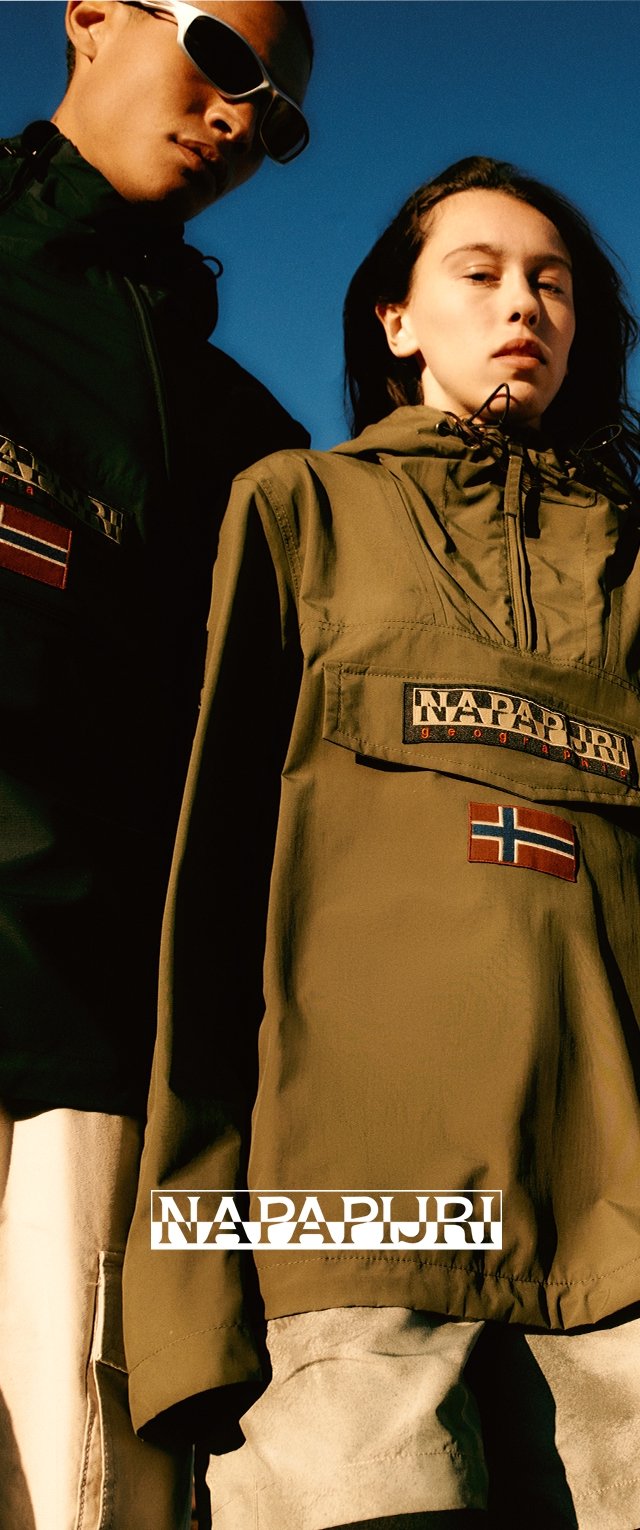 Khakifarbene Pull-Over-Jacke mit Reißverschluss am Hals, großem Logo-Patch und norwegischer Flagge. Modell in leichter schwarzer Jacke mit Sonnenbrille.