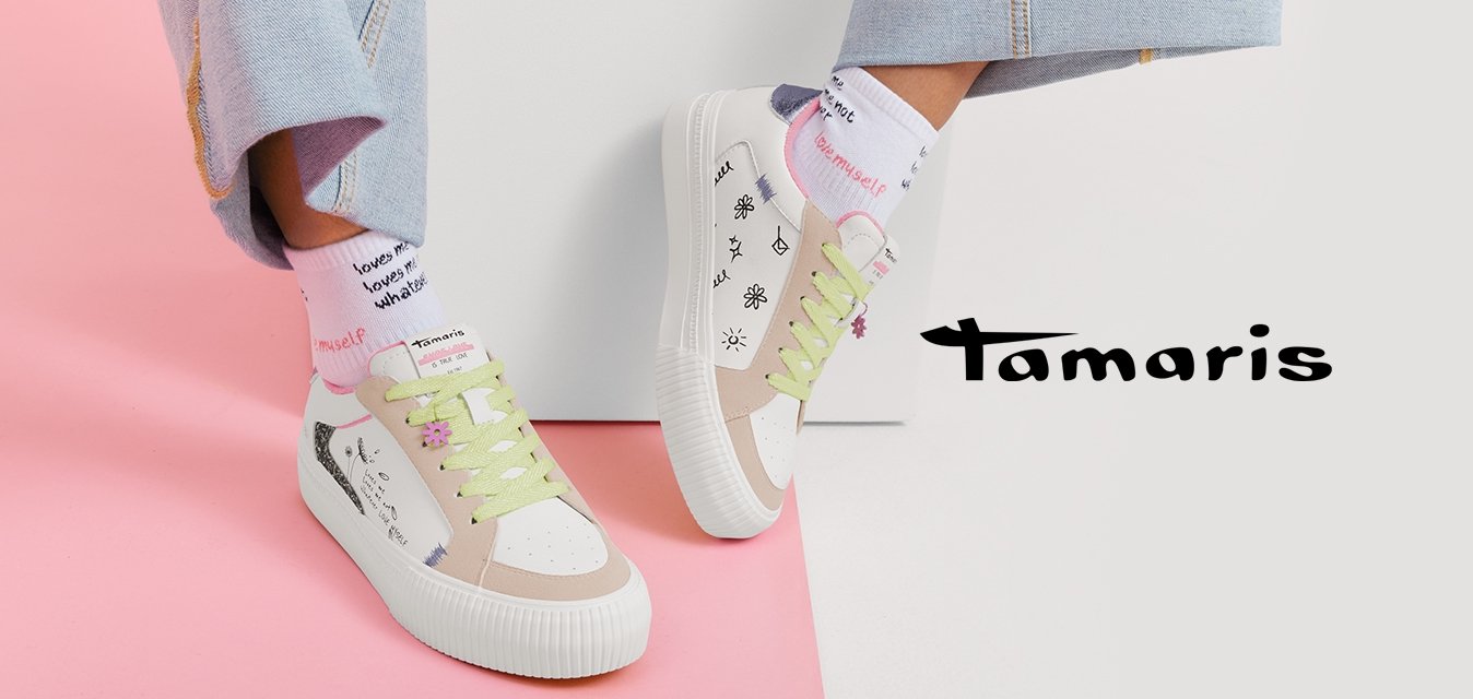 Osoba nosící světlé džínové kalhoty, bílé tenisky s pastelově zelenými tkaničkami a ručně psanými vzory a bílé ponožky s červeným textem.