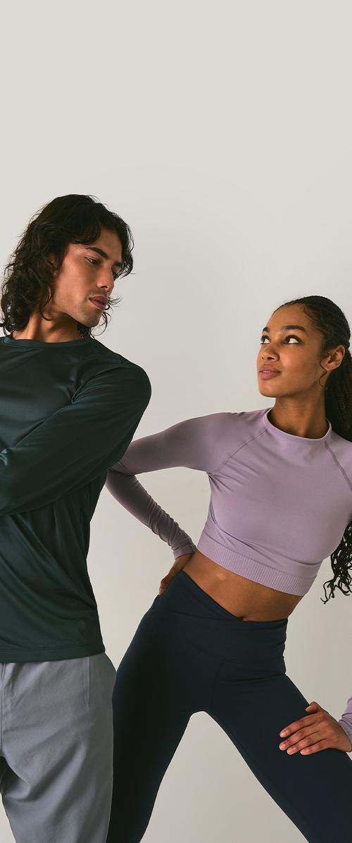 Modelo vistiendo una camisa de manga larga ajustada de color verde oscuro, pantalones grises; otro modelo con un top corto de color púrpura claro y leggings navy de cintura alta.