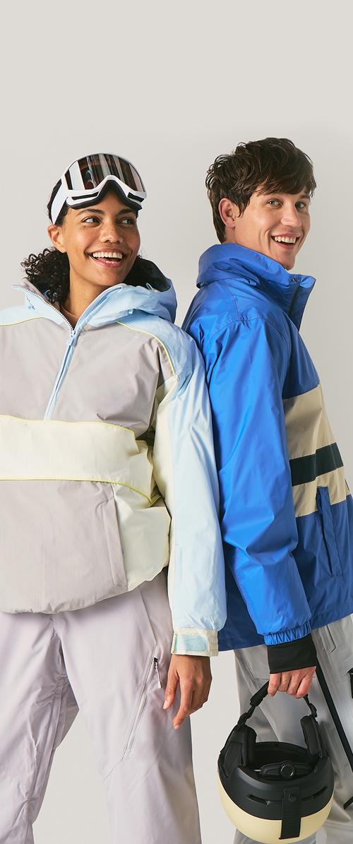 Chaquetas de invierno coloridas: una gris con detalles amarillos y una azul con rayas negras. Ambas cuentan con cremalleras y capuchas; un modelo sostiene un casco.