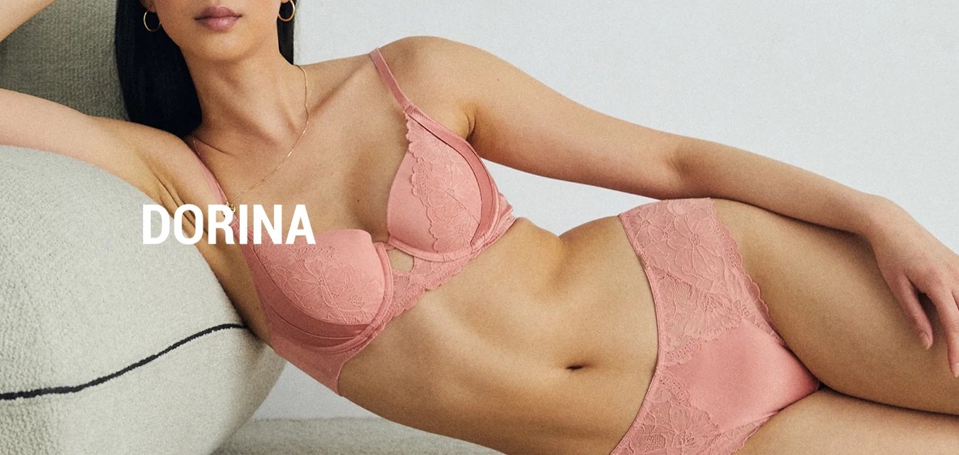 Růžová krajková podprsenka a odpovídající kalhotky s květinovými vzory, měkkou tkaninou a jemnými pásky, umístěné na světlém koberci s pohovkou.